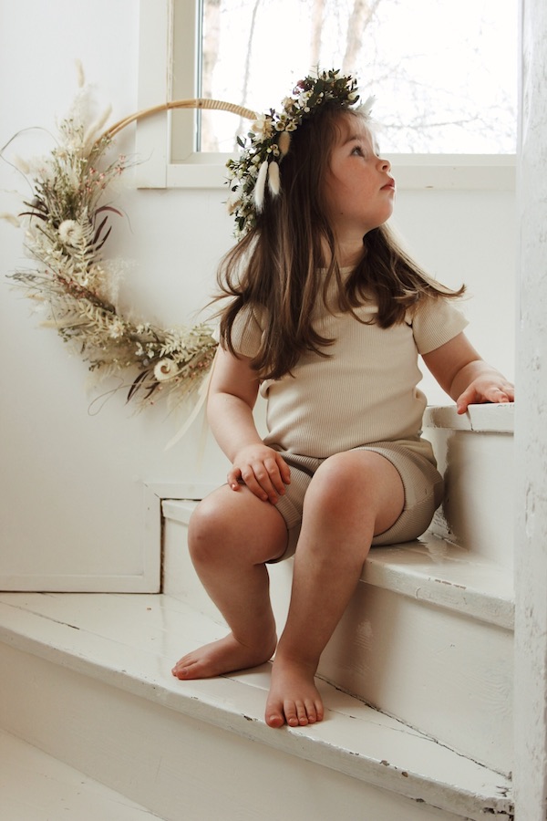 Tyttö istuu portaikossa kukkaseppele hiuksissaan ja yllään Aito T-paita ja Aarre Shortsit