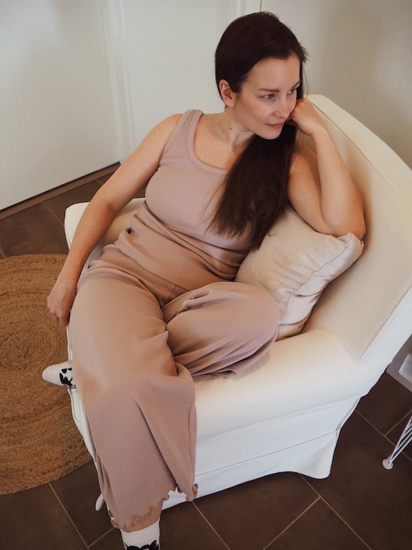 Nainen istuu nojatuolissa roosan sävyisessä ribbi topissa ja culottes housuissa