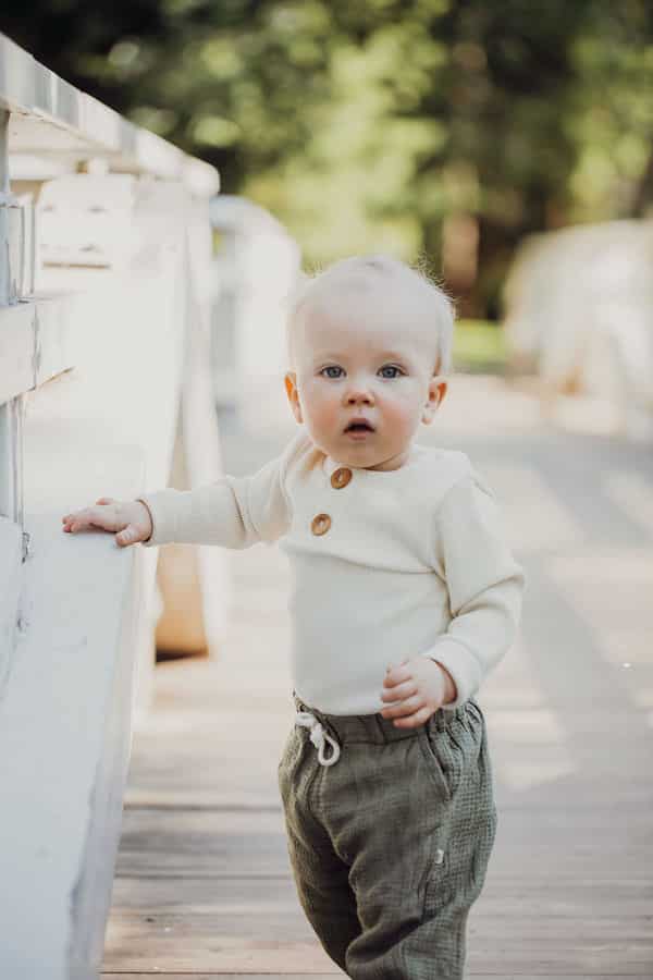 Vauva seisoo sillalla yllään valkoinen ribbi body ja vihreät pellava housut