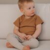 Poika istuu vaalealla sohvalla karamellin ruskeassa t-paidassa ja pellavan ruskeissa legginsseissä.