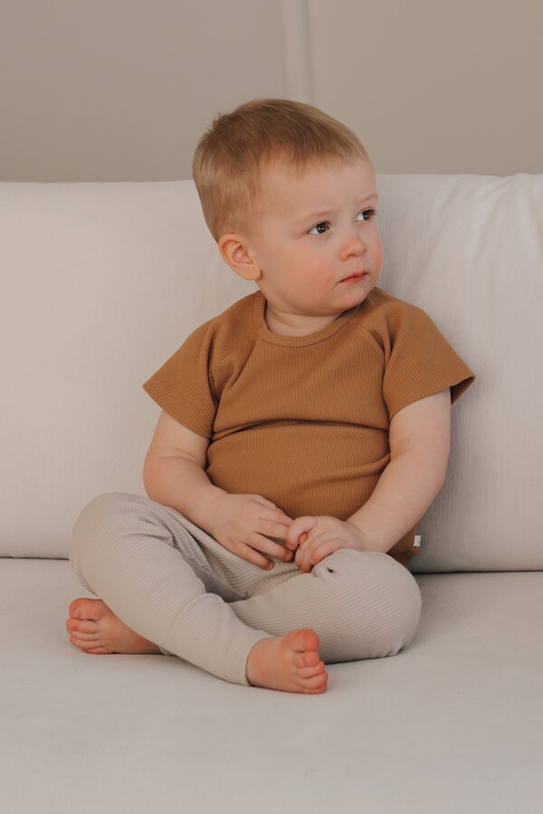 Poika istuu vaalealla sohvalla karamellin ruskeassa t-paidassa ja pellavan ruskeissa legginsseissä.